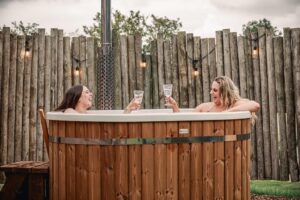 Friends on a hen weekend enjoying a drink in the Aster cabin wood-fired hot tub