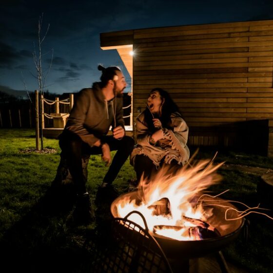 Couple toasting marsh-mallows in the dark over a roaring fire-pit at the meadows at polehanger